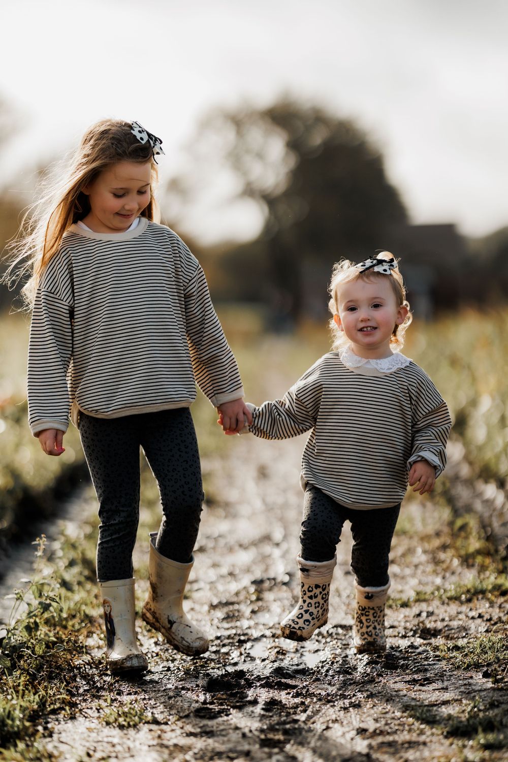 Two people in matching striped sweaters walking together down a muddy path.