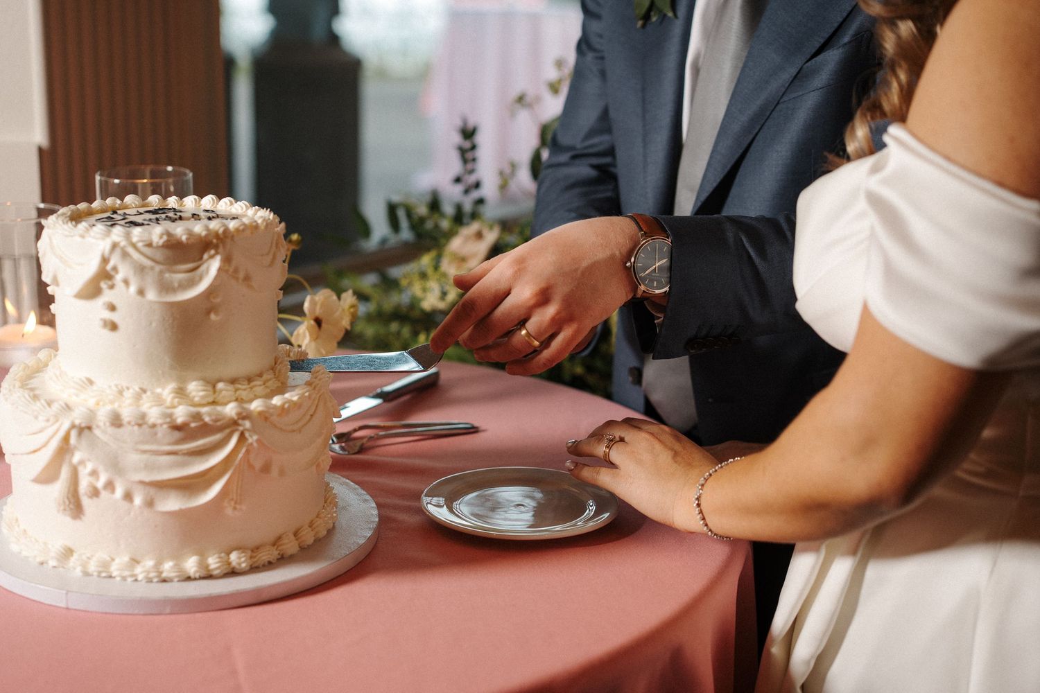 Couple slices elegant white wedding cake covered in delicate floral decorations on pink tablecloth.