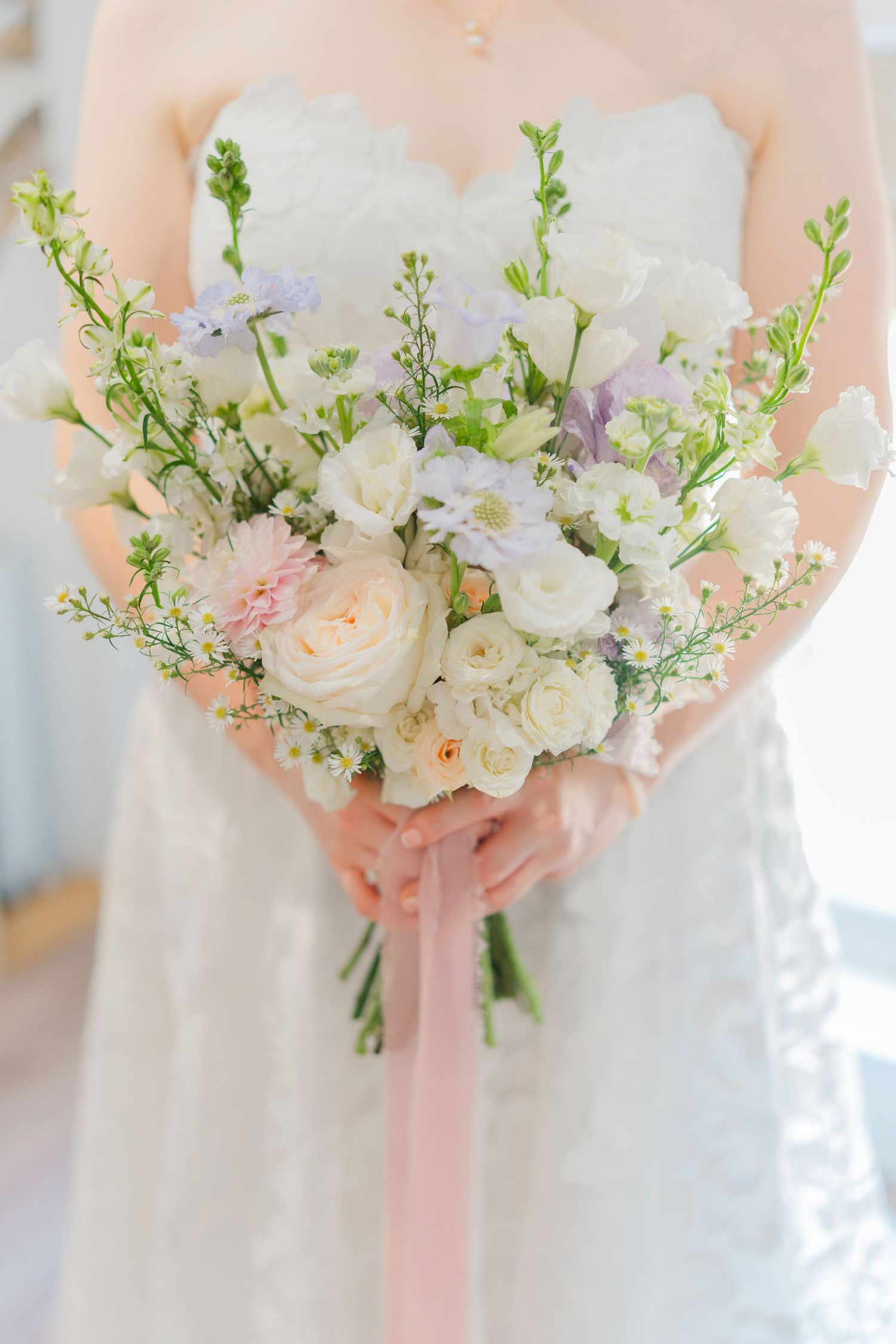 A delicate bridal bouquet of white roses and wildflowers tied with a pink ribbon.