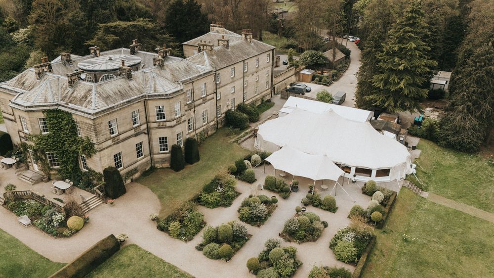 Aerial panoramic view of a historic estate with manicured gardens, circular driveway, and surrounding greenery.