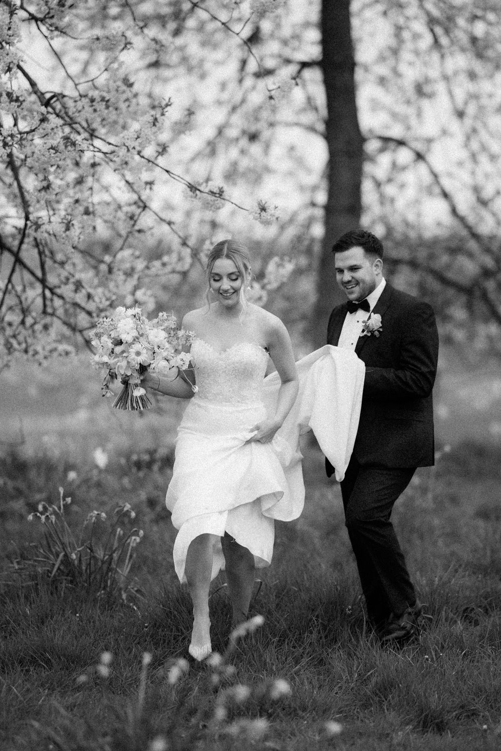 A black and white wedding photo captured under blooming spring trees.
