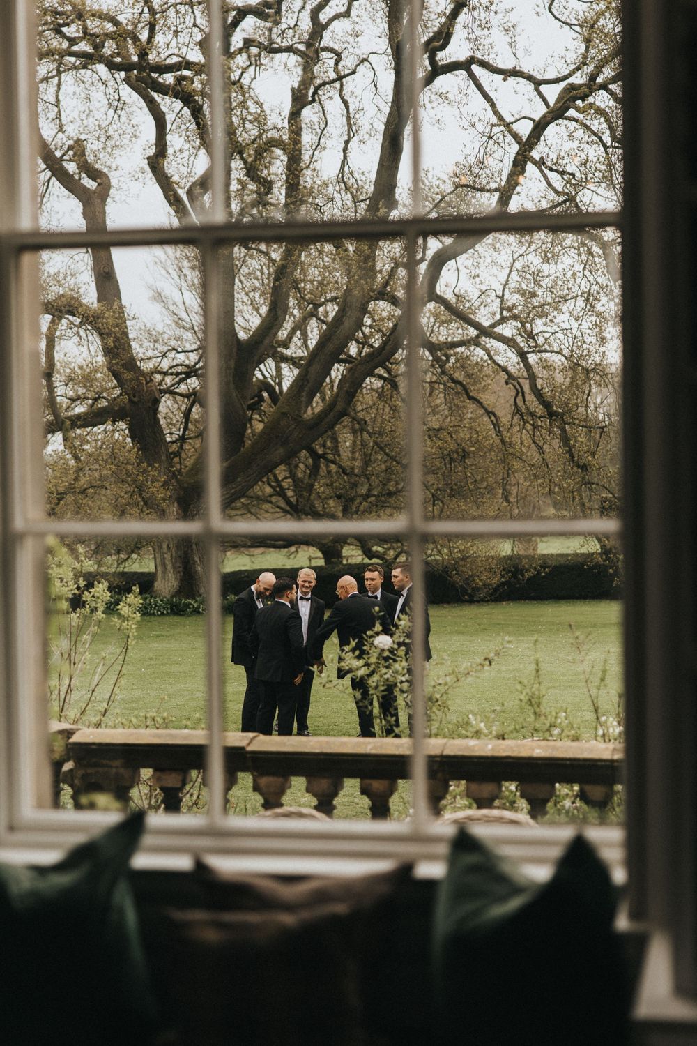 A window view looking out onto a garden with people gathered under bare winter trees.