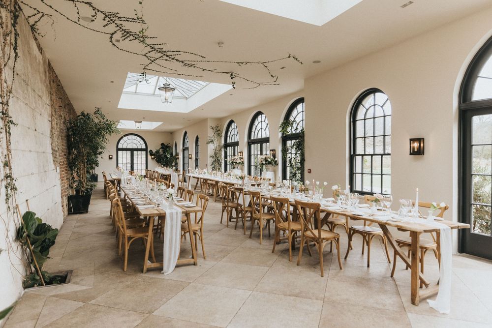 Elegant wedding reception venue with arched windows, natural light from skylights, and rustic wooden tables decorated for dining.