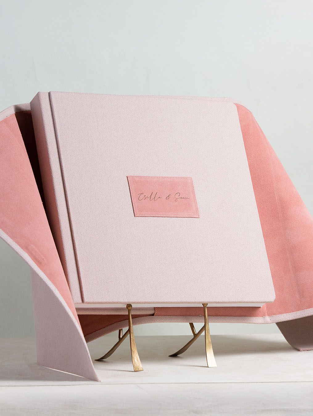 Close-up views of pastel pink bound book or album with golden stand displayed at different angles in minimal setting.