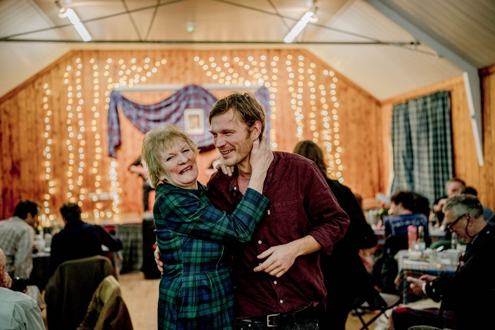 Two people dance and laugh together at an indoor event with twinkling string lights decorating the venue behind them.