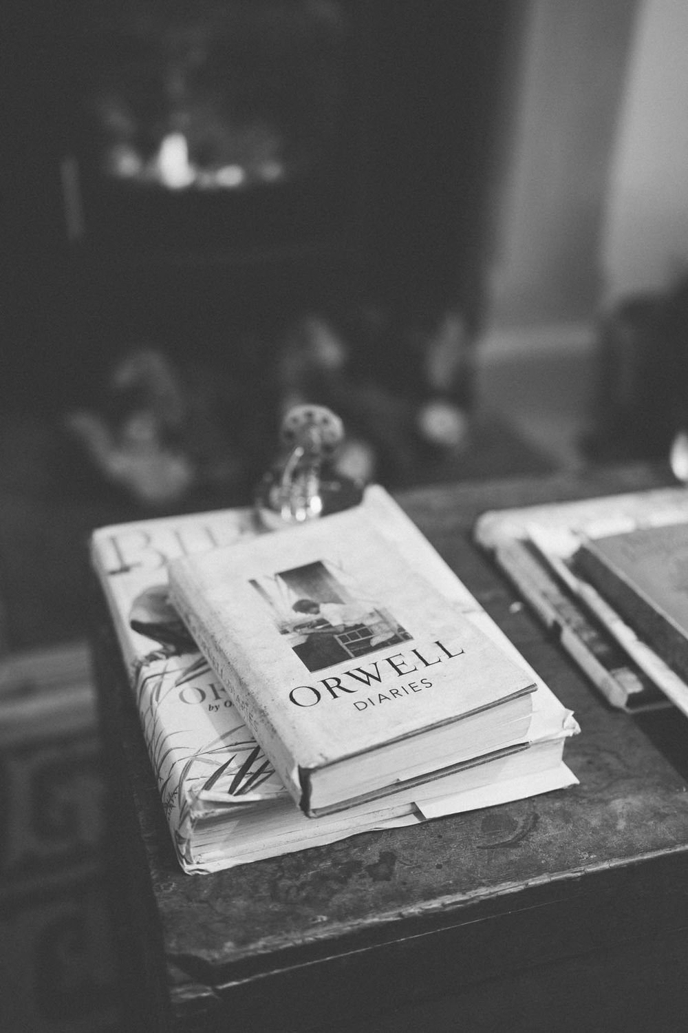 Black and white photograph of stacked books including an Orwell title on a weathered wooden surface in moody lighting.