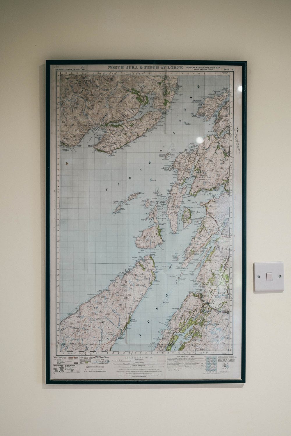 A framed vintage map showing coastal regions of Scotland displayed on a white wall next to a light switch.