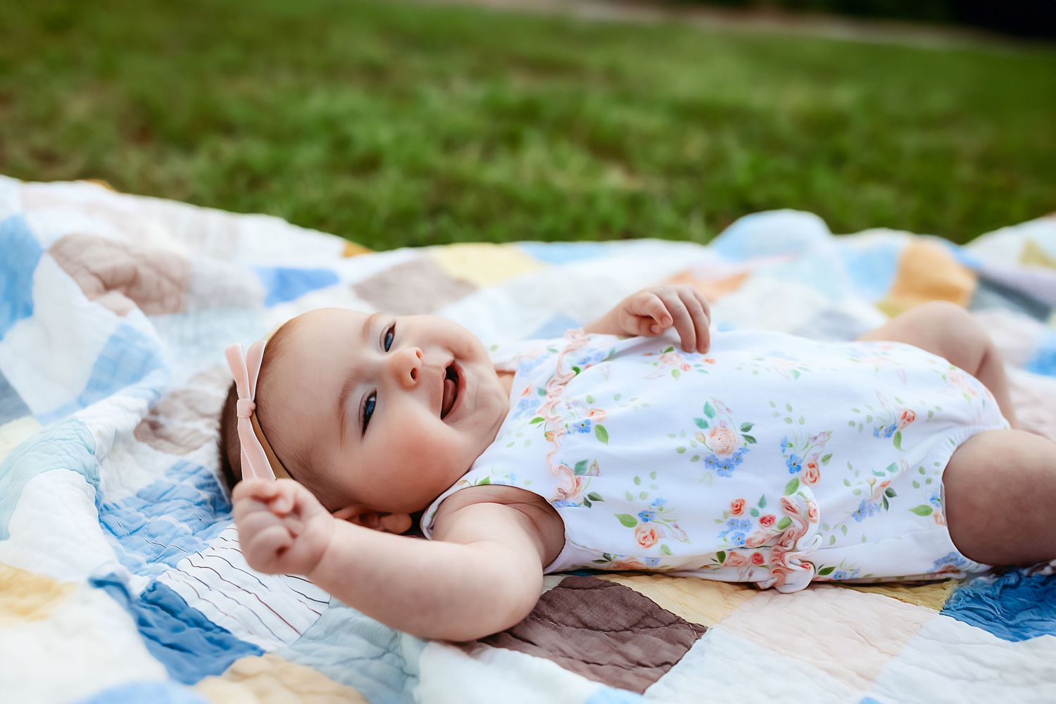 A baby wearing a floral print outfit lies on a blue blanket during an outdoor photography session.