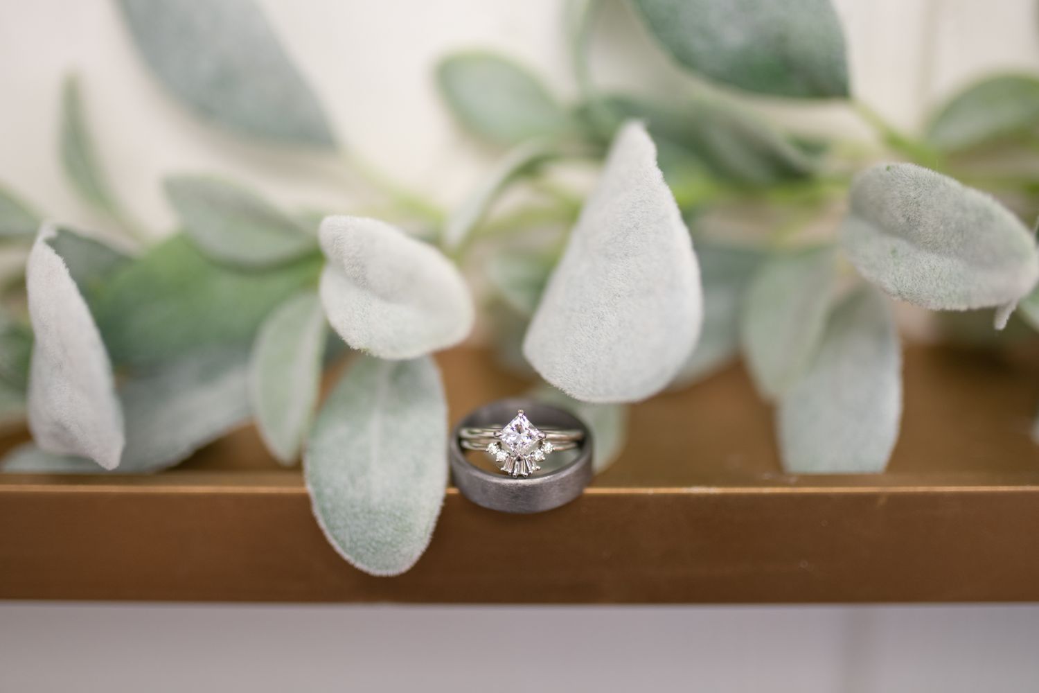Wedding rings displayed artistically on wooden surface with soft eucalyptus leaves.