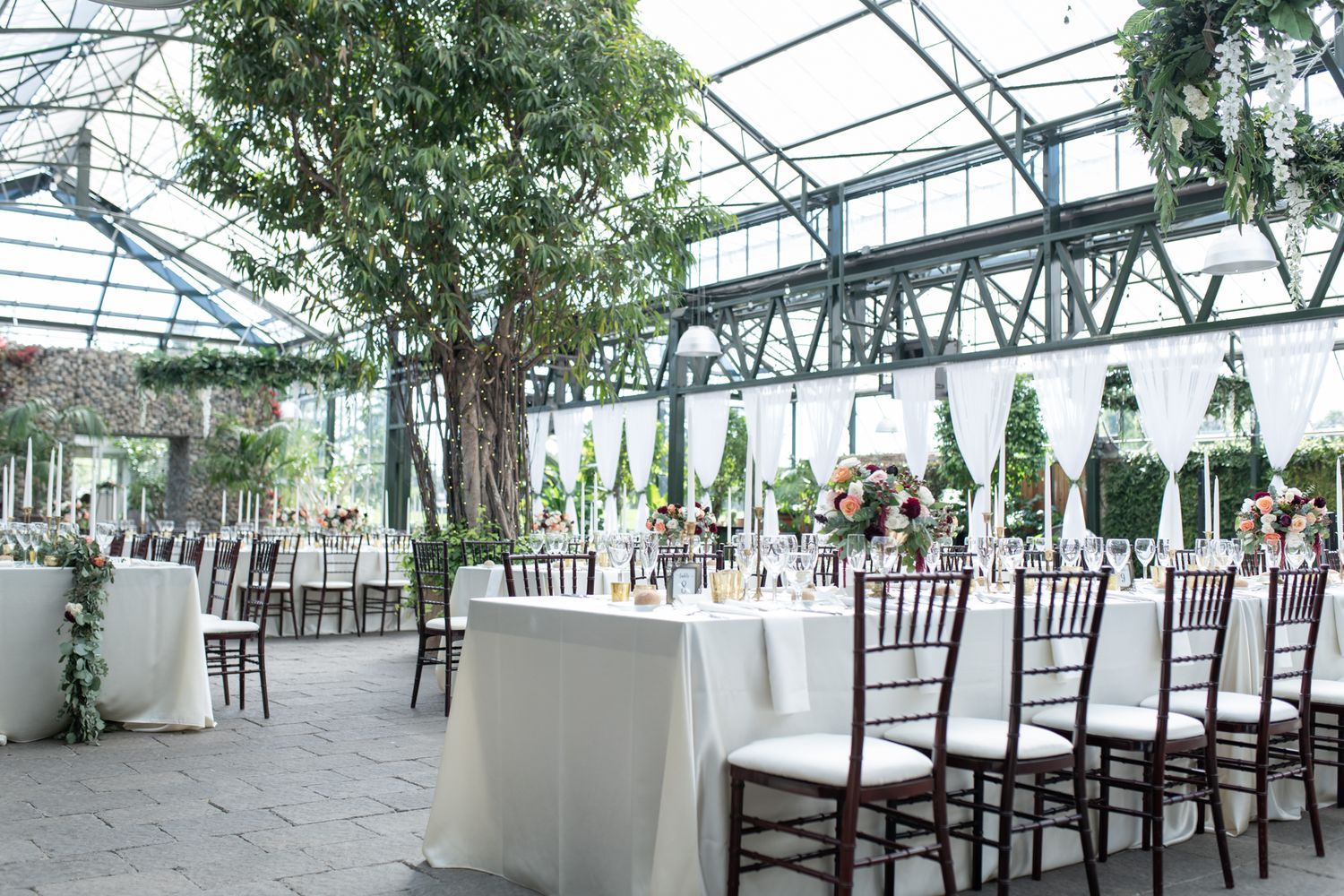 Modern greenhouse wedding reception venue with white tables and chiavari chairs set for dinner.