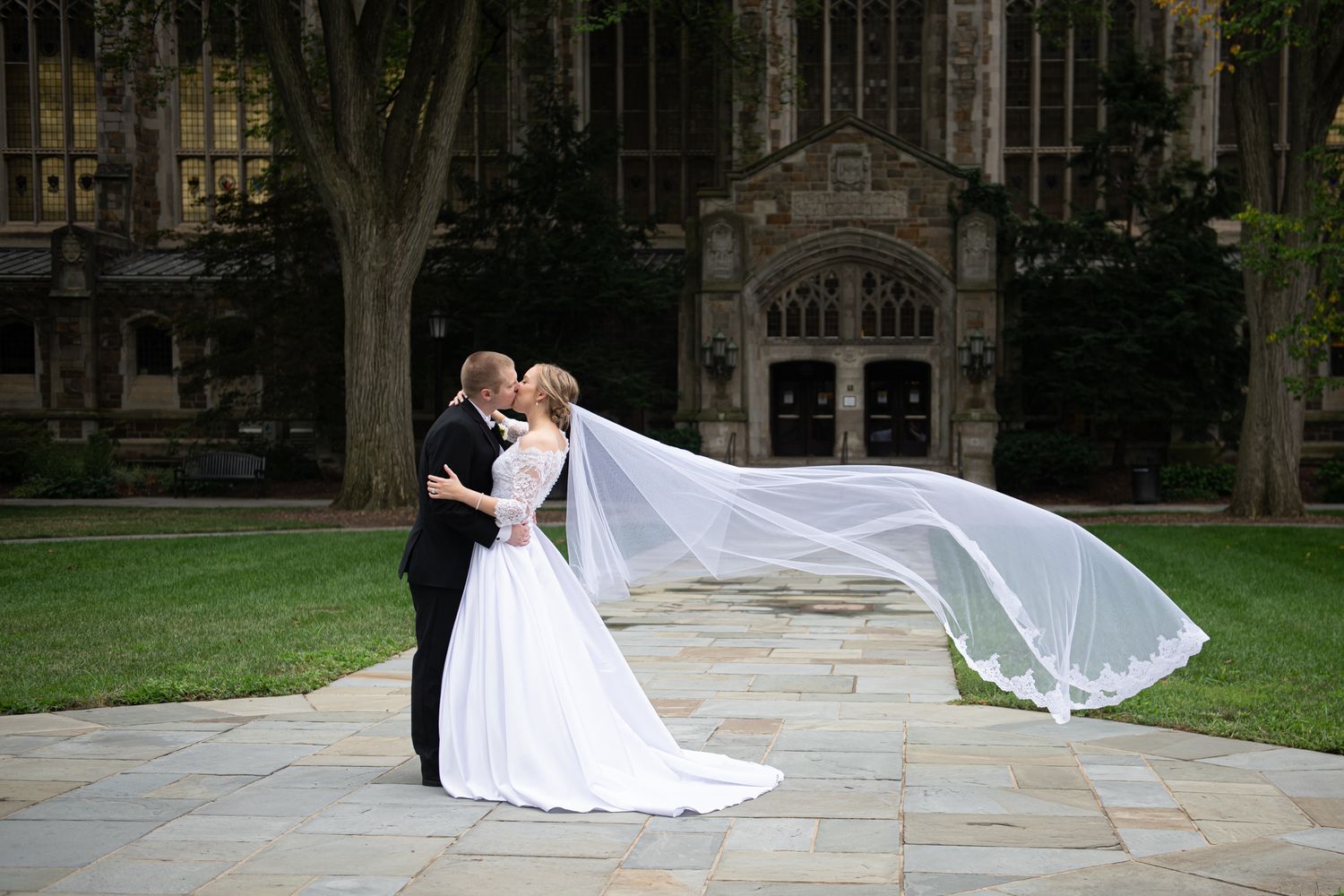 A romantic outdoor wedding portrait set with a couple in traditional attire kissing under scenic stone architecture.