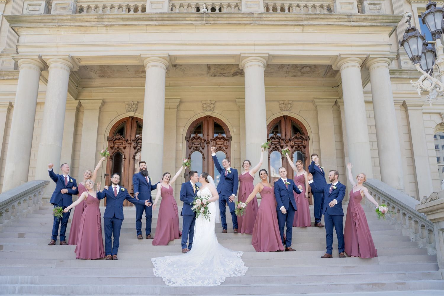 Wedding party celebrates on grand stone steps of classical building with pink and navy color scheme.