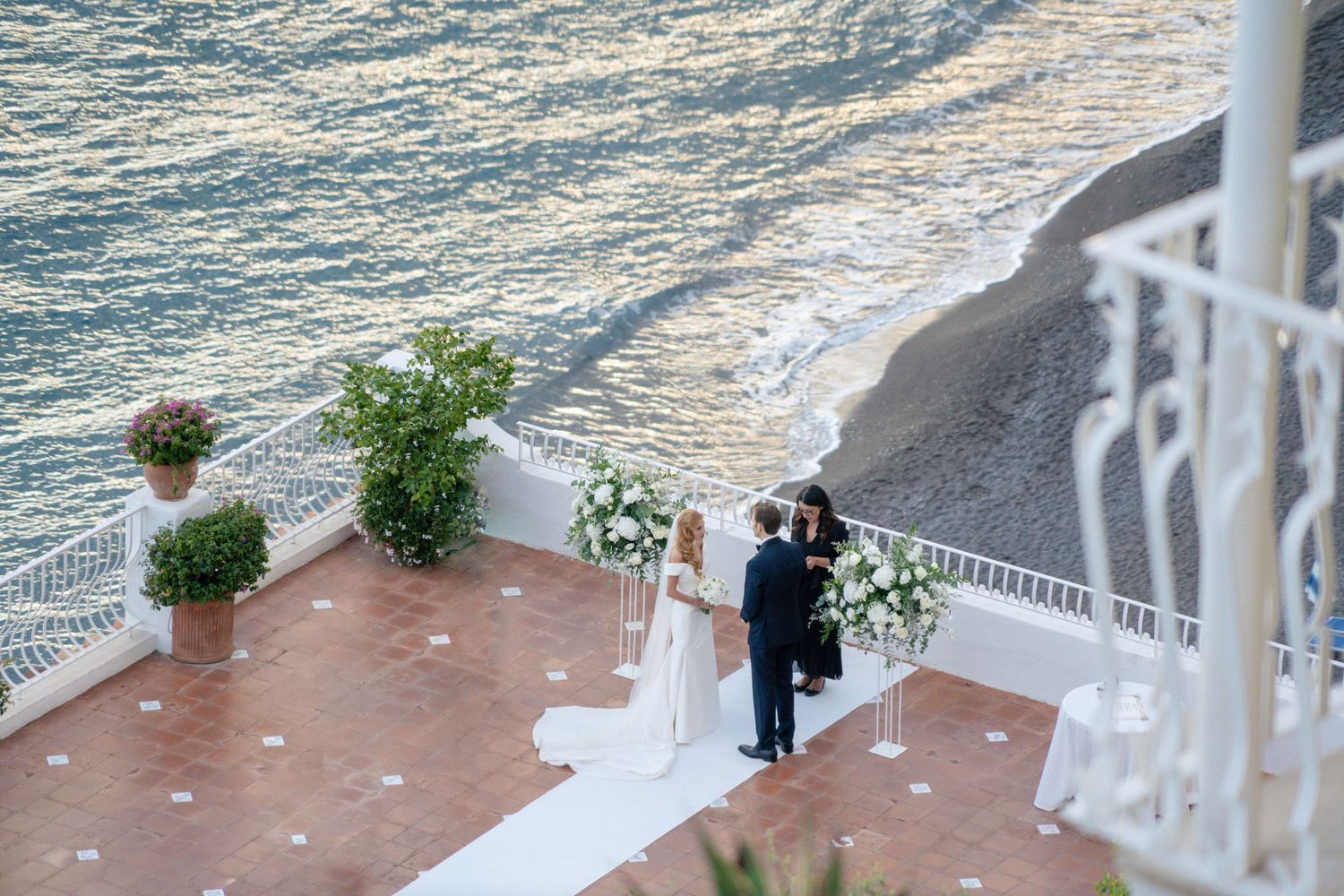 Aerial view of wedding ceremony on coastal terrace overlooking ocean.