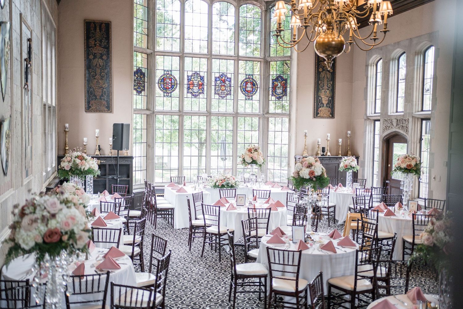 Elegant wedding reception venue with tall windows, chandeliers, and round tables set with pink and white decor.