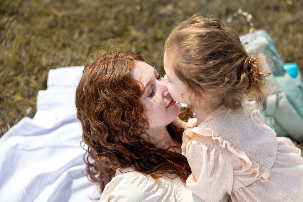 Parent and child lying on white blanket outdoors sharing joyful laughter during intimate candid moment.
