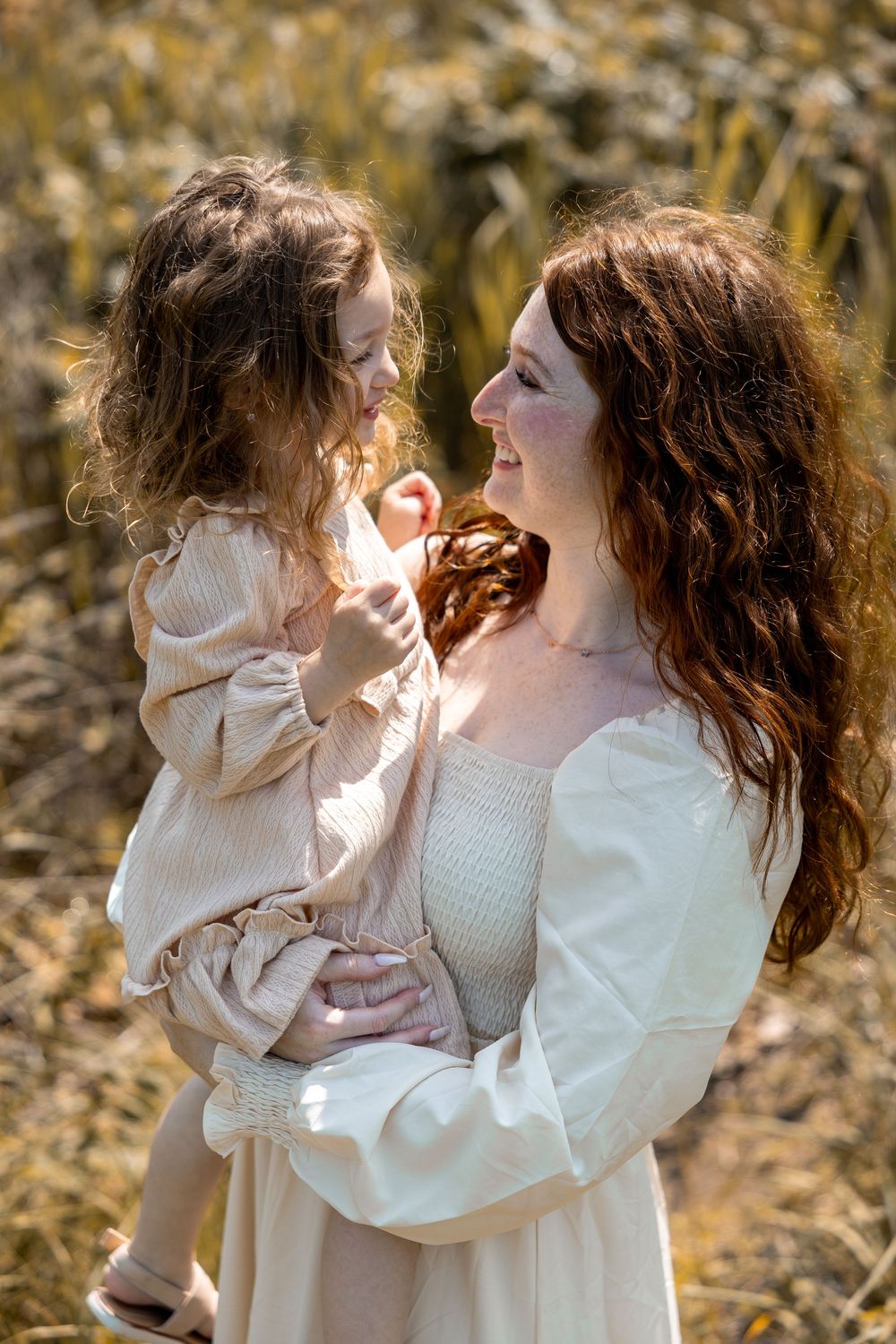 A tender outdoor portrait of figures wearing matching cream-colored dresses against a natural autumn background.