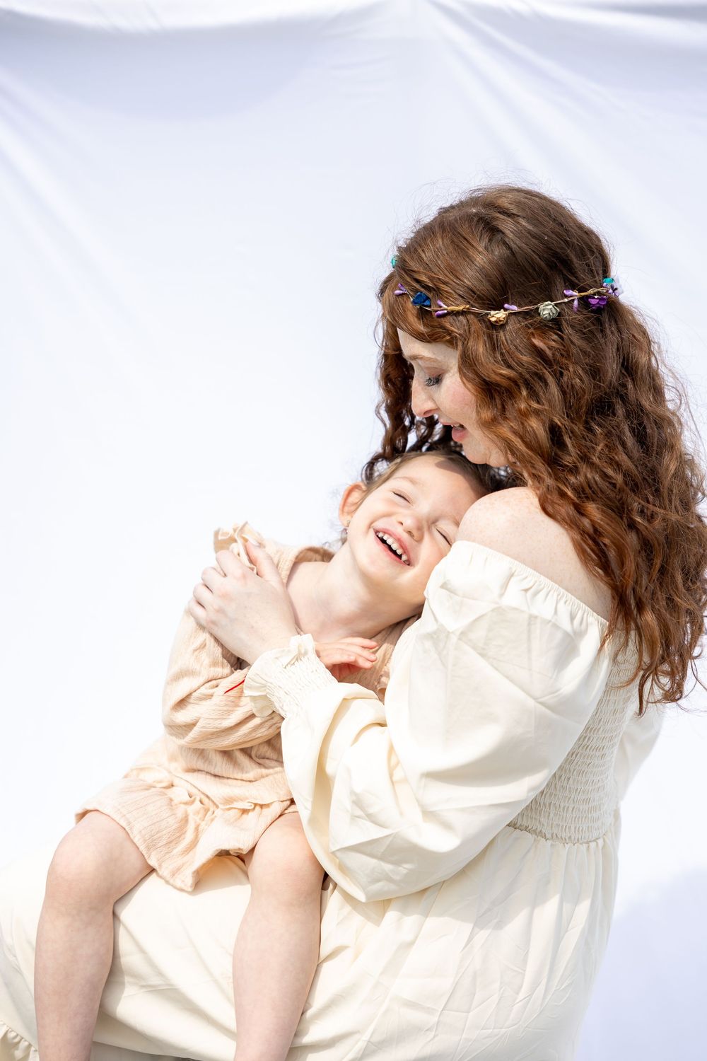 A person with curly brown hair wearing a cream colored blouse poses gracefully against a white background in a photo series.