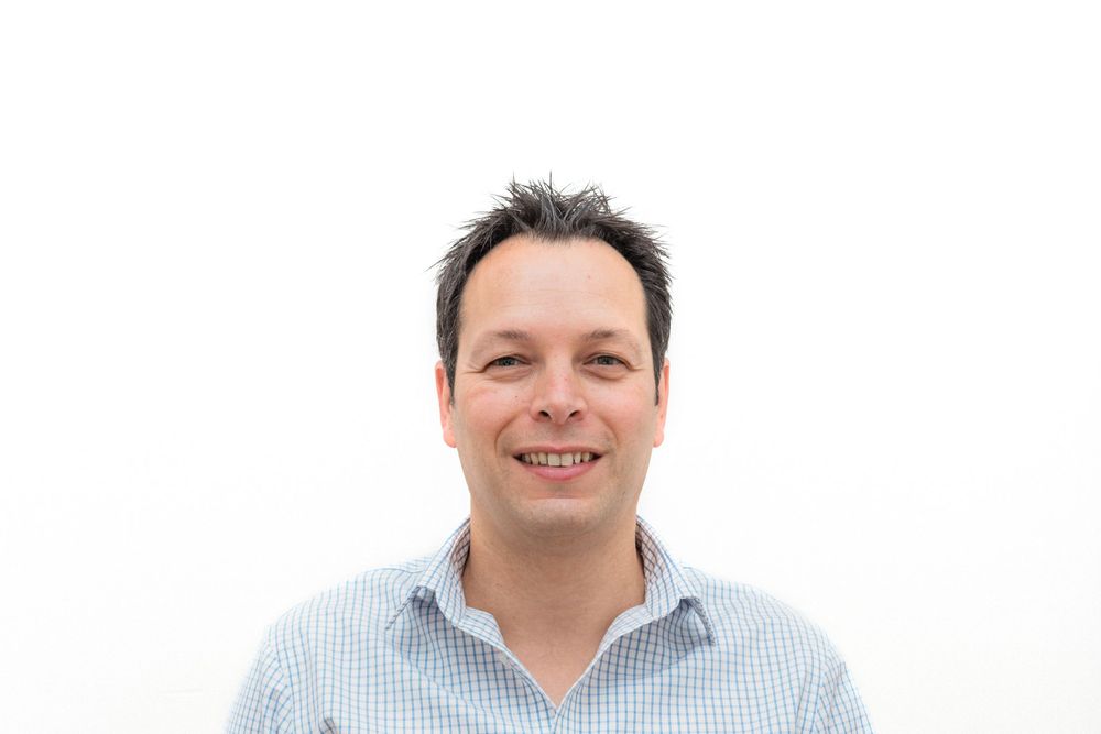 Headshot of a person wearing a light blue checkered button-down shirt against a white background.