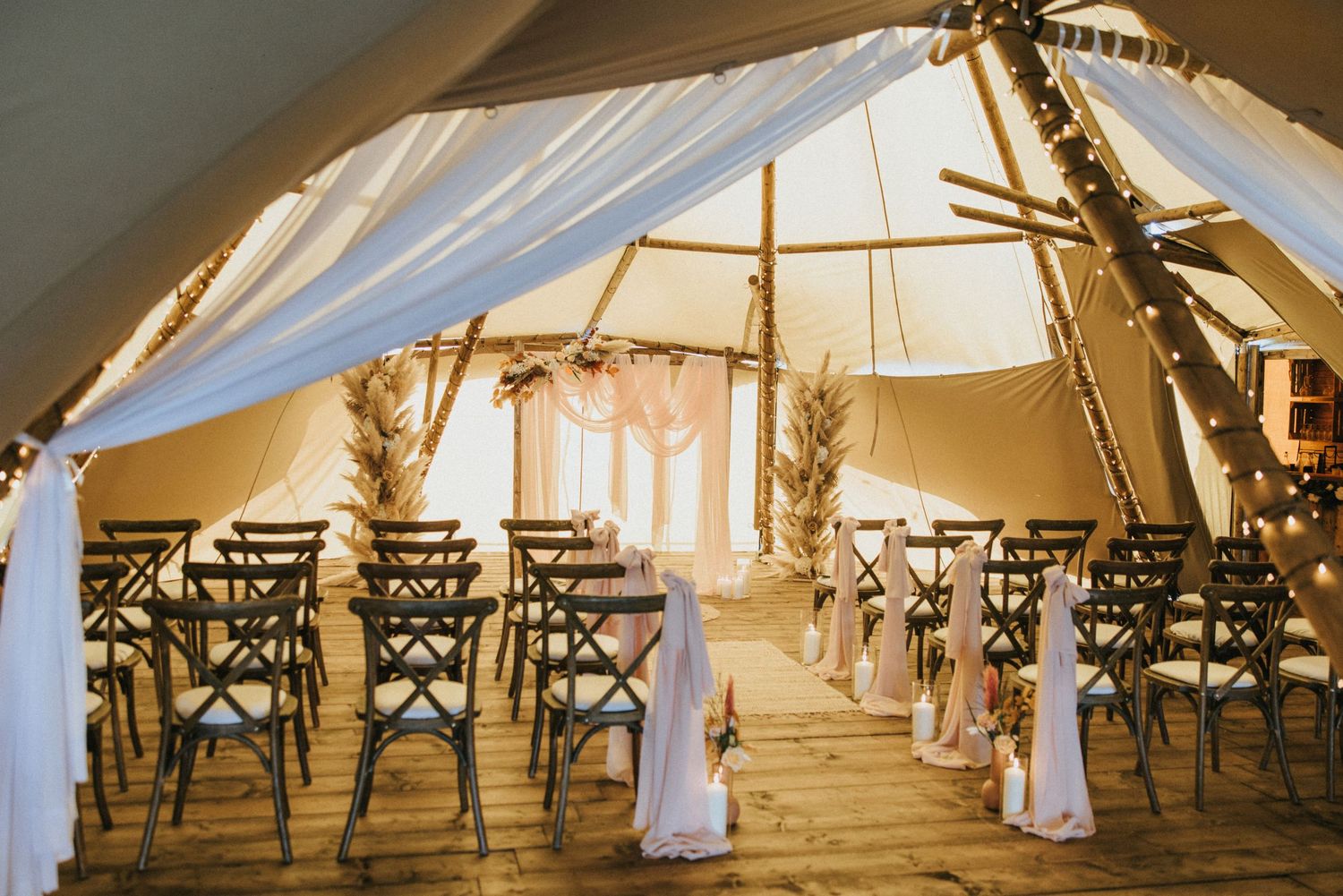 Interior of an elegant rustic wedding tent with wooden chairs set up in rows for a ceremony at Nuddock Wood Lake.