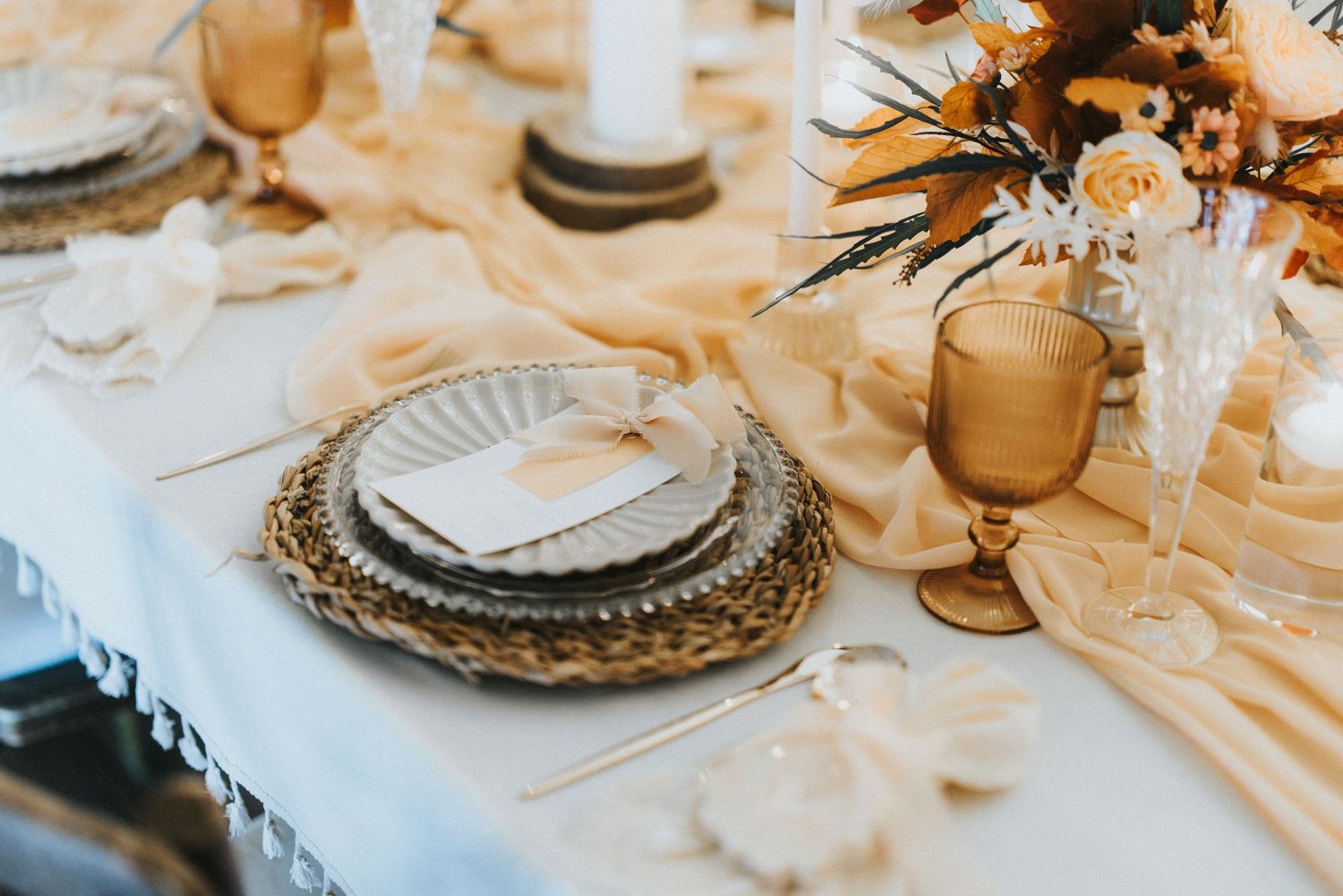 Elegant table setting with woven charger plates, amber glassware and floral centerpiece on cream linens at Nuddock Wood Lake.