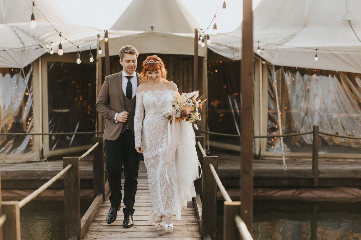 A couple walks down rustic wooden steps outside of a large canvas tent at an outdoor wedding venue at Nuddock Wood Lake.