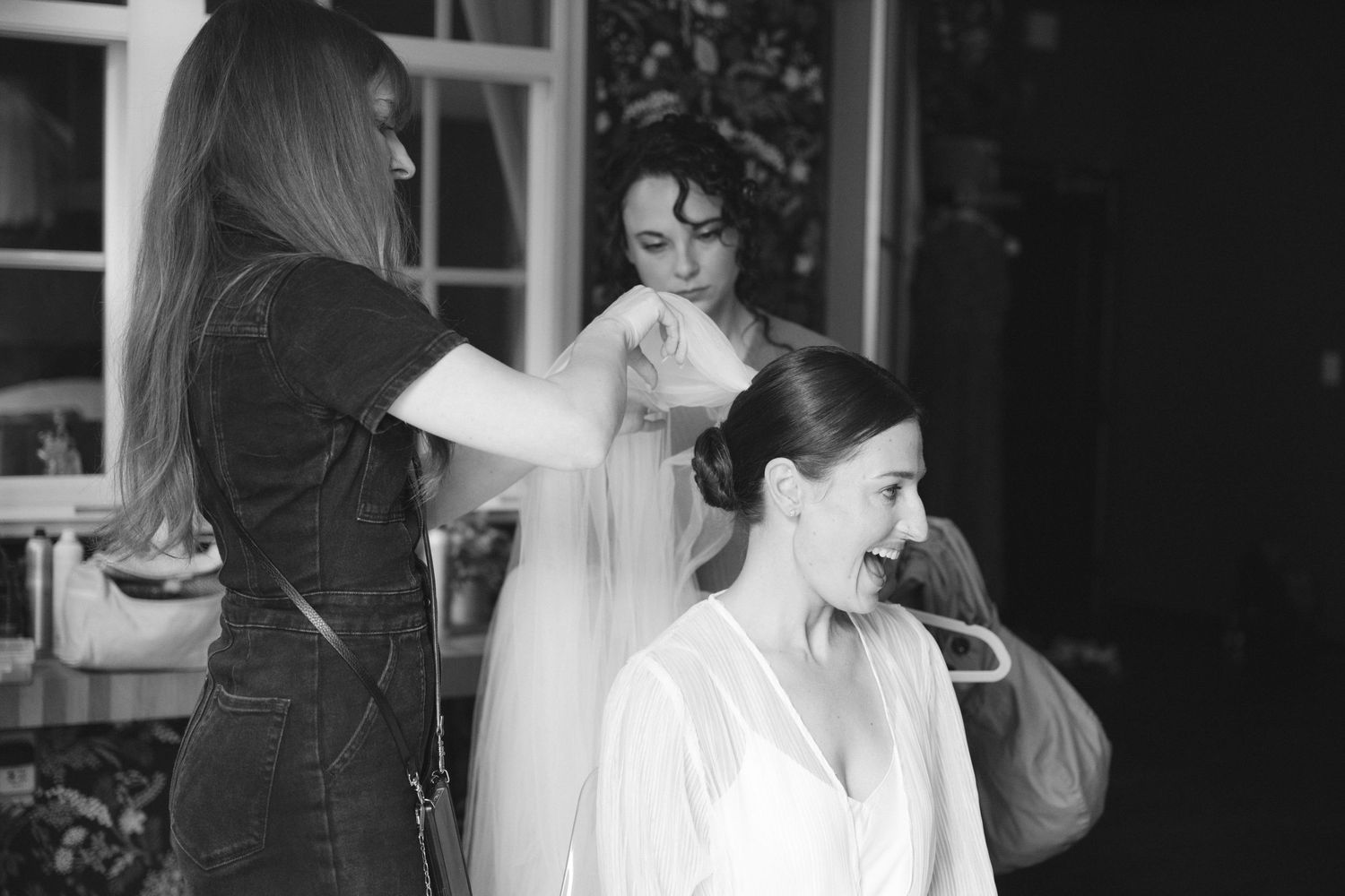 Black and white photograph of a bride getting ready for her wedding surrounded by helpers in a preparation room.