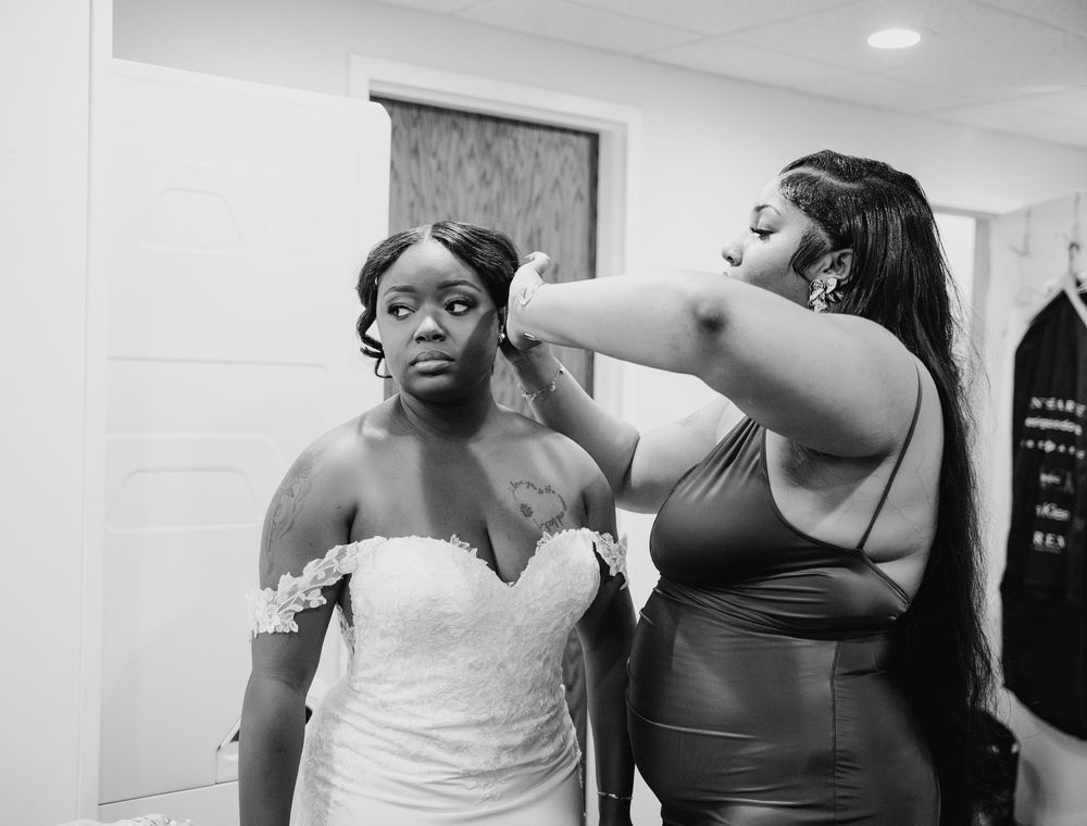 A person in a white wedding dress gets help with styling preparations in a dressing room.