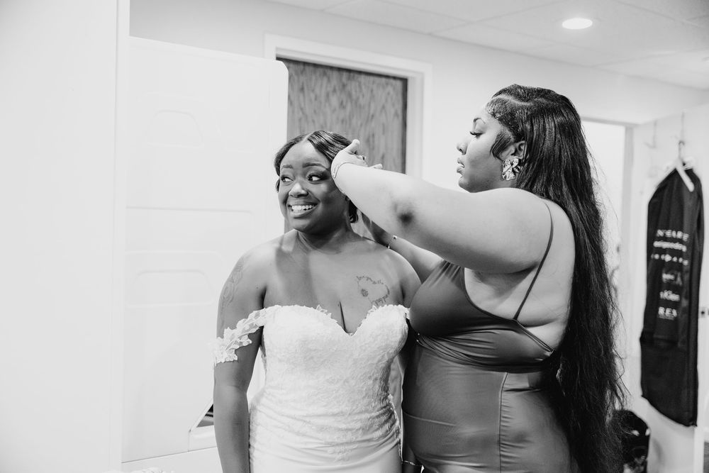 A joyful moment of getting ready before a wedding, as someone helps adjust another's dress in a black and white photo.