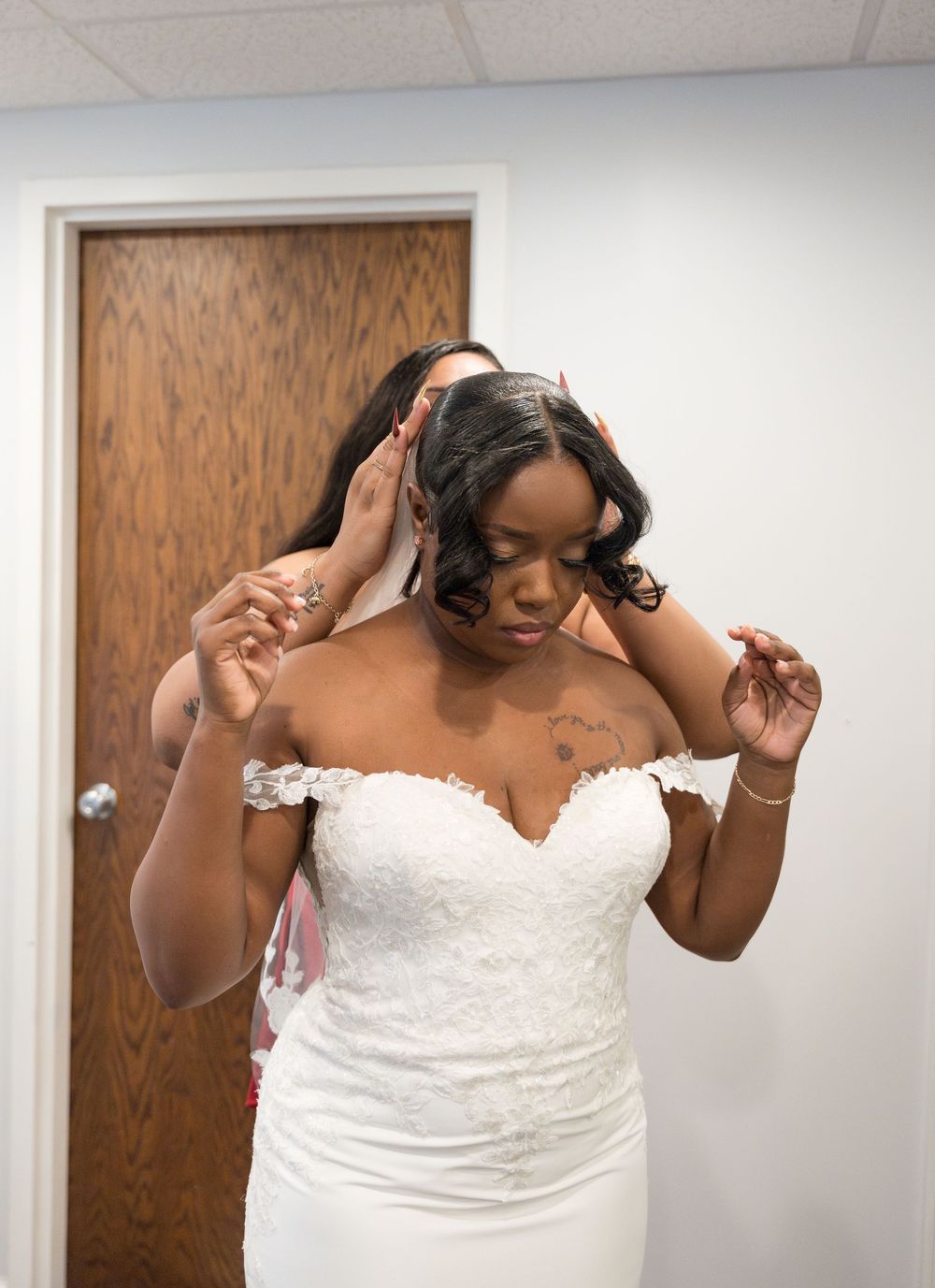 Sequence showing a bride in a white strapless lace wedding gown getting ready in a fitting room.