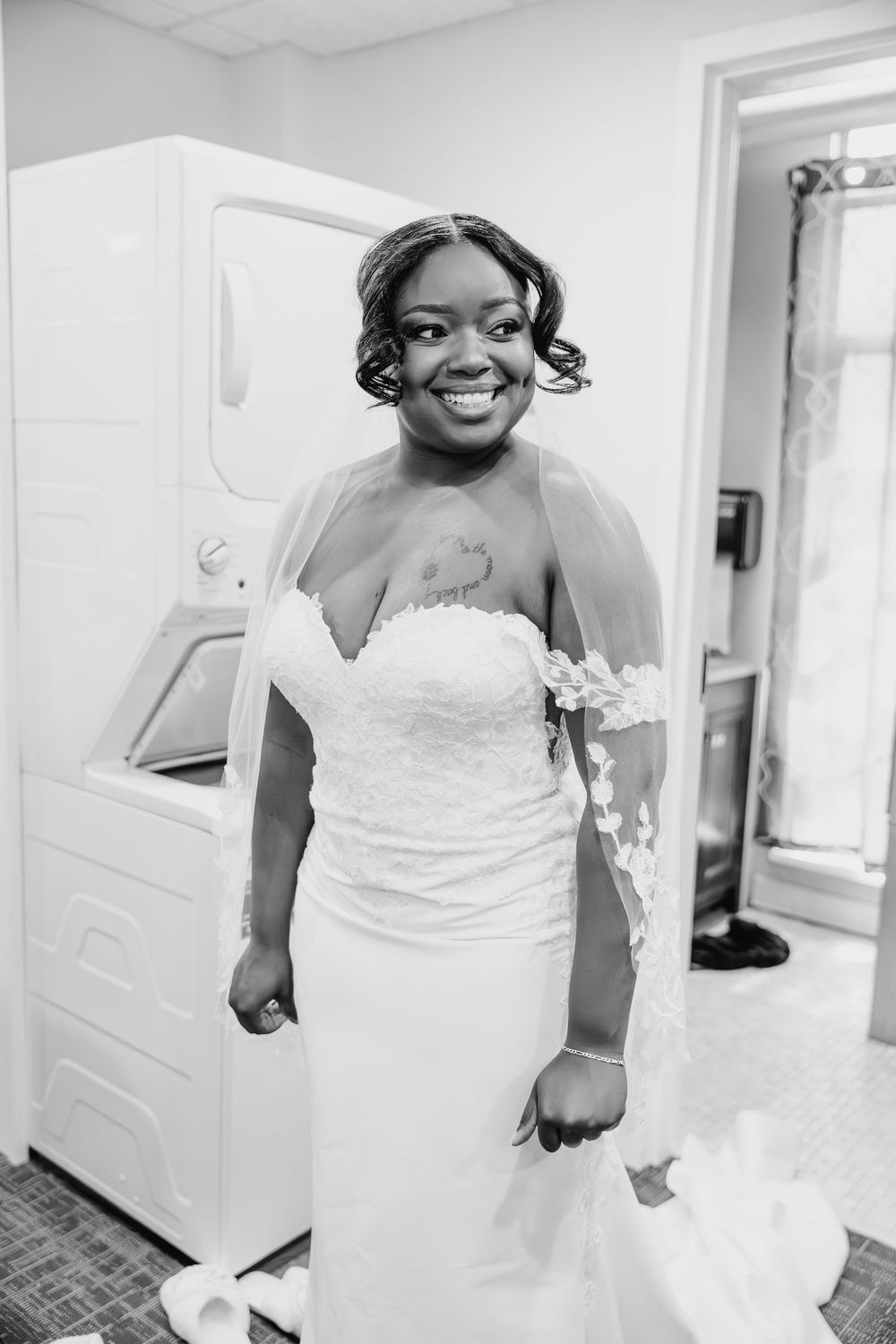 A joyful bride in an elegant strapless white wedding gown smiles radiantly in a black and white photograph.