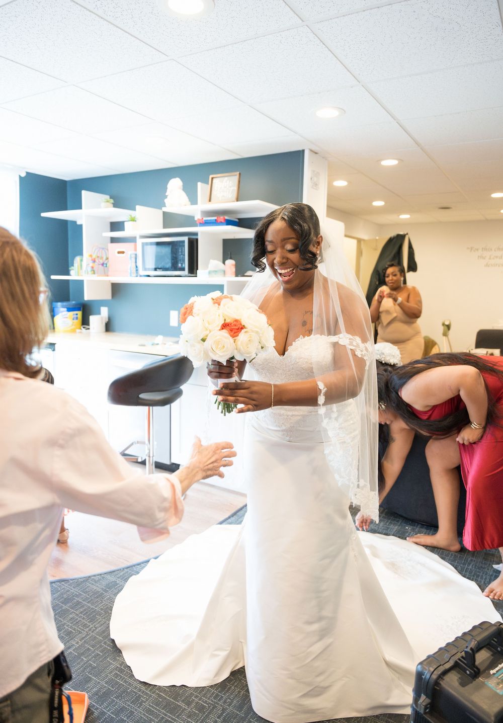 A bride wearing a white wedding dress stands in a dressing room during final preparations for her special day.