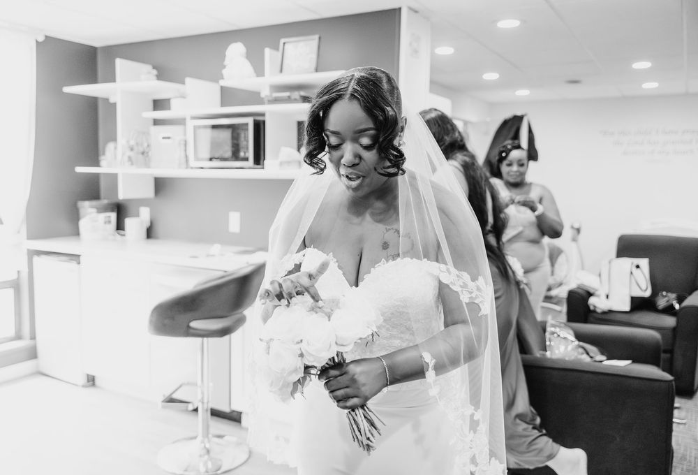 A black and white photo showing a bride in veil and gown holding a bouquet in a modern salon setting.