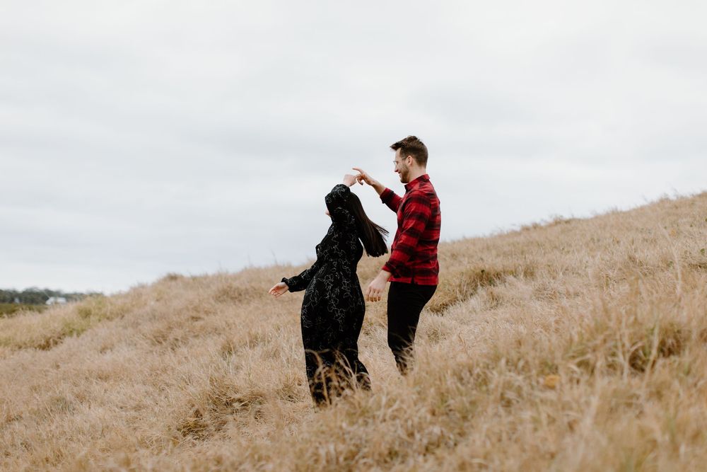 Couple playing and laughing together on windswept hillside.