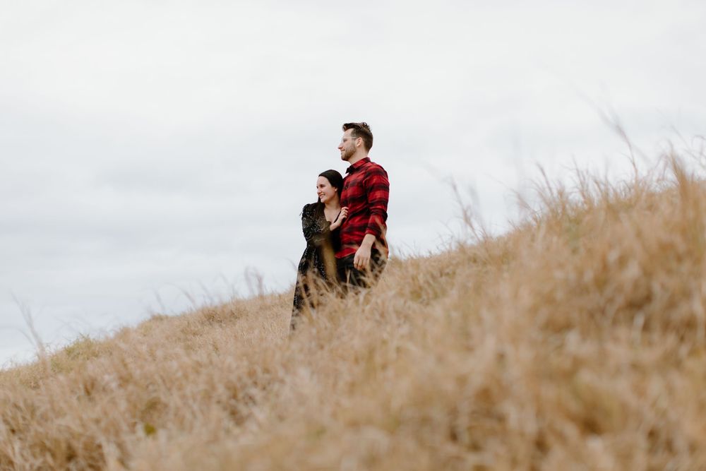 Romantic couple standing in distance on grassy hilltop.