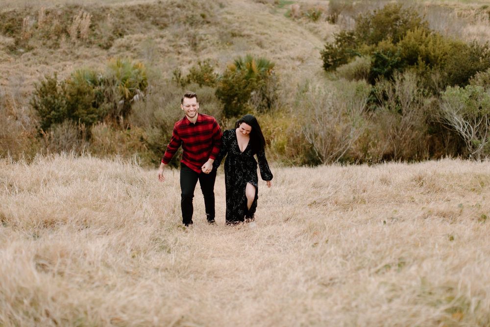 Couple walking together through tall grass on hillside.
