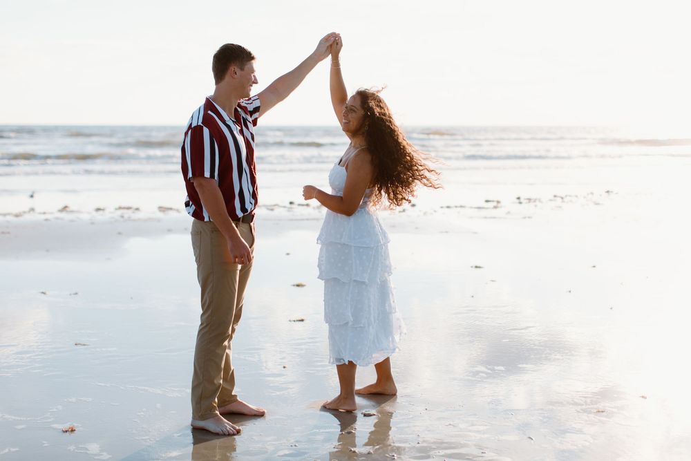 Couple dancing together on a sandy beach during golden hour.