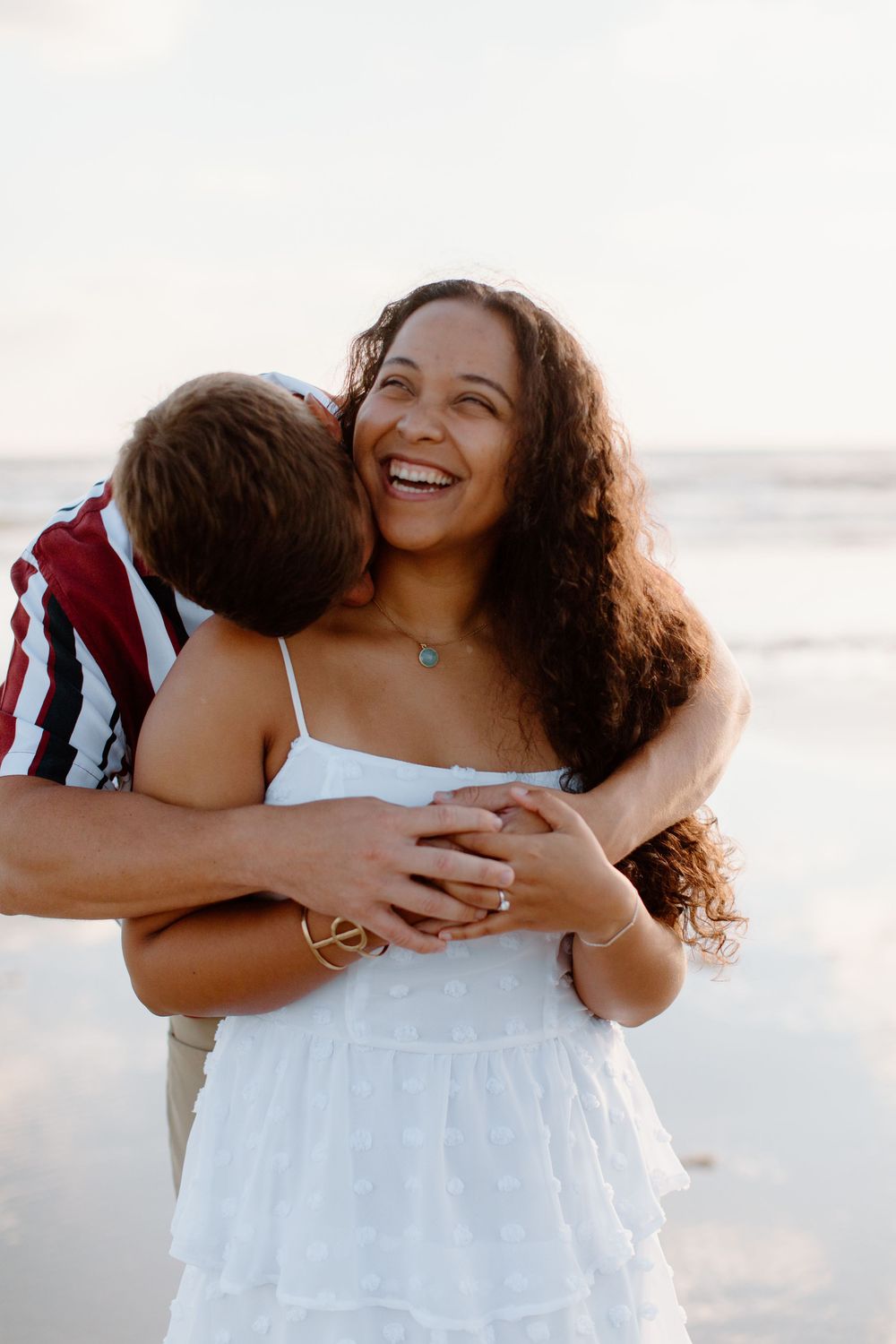 Couple shares a warm embrace and laughter on the beach at sunset.