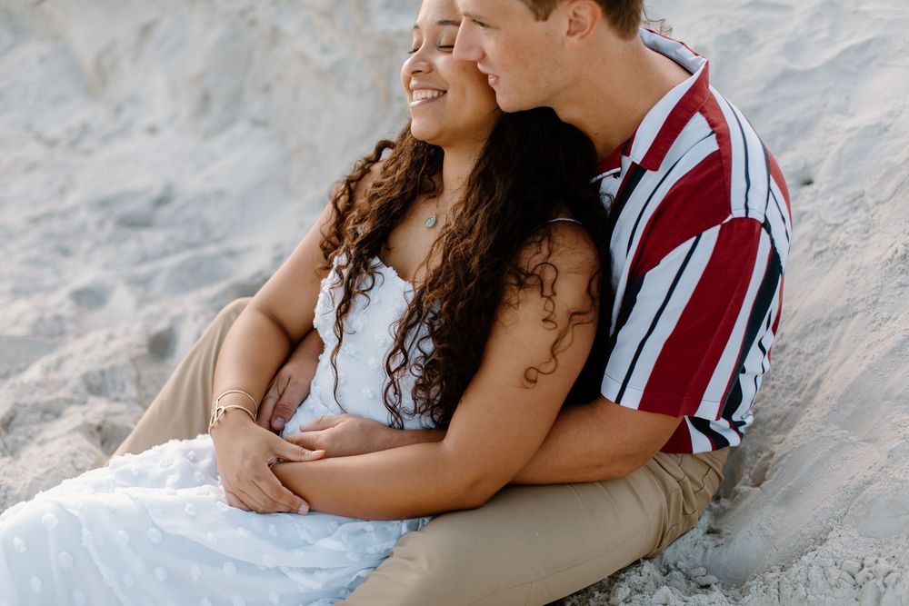 Couple cuddling on sandy beach during romantic sunset photoshoot.