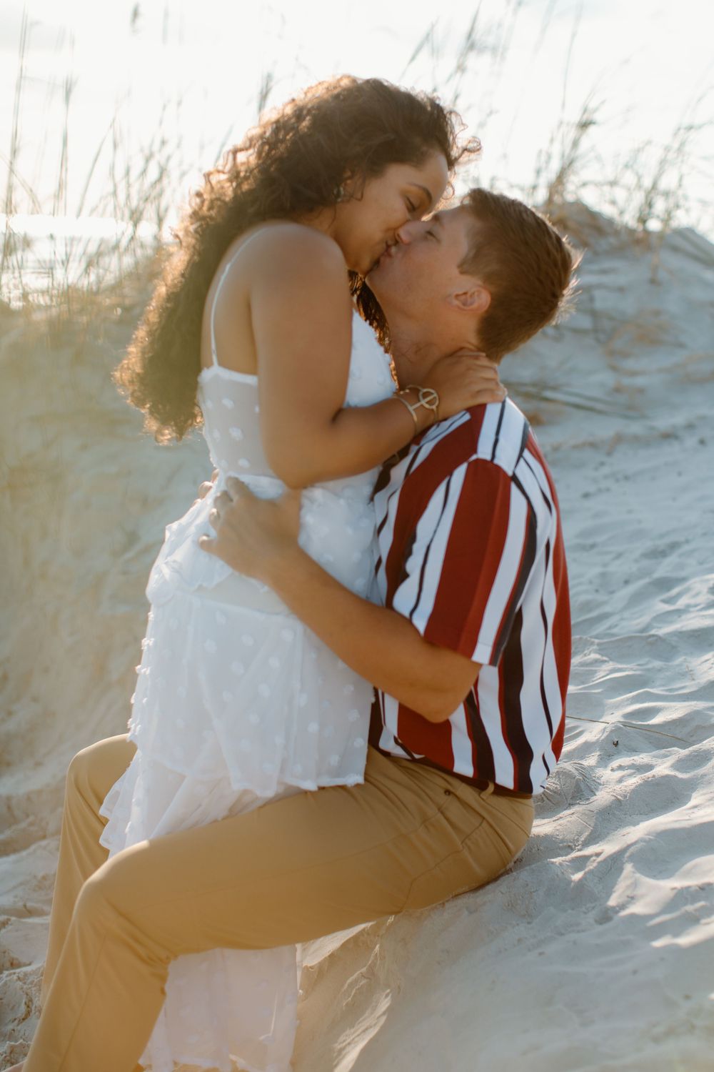 Couple embracing passionately on sandy dunes during golden hour.