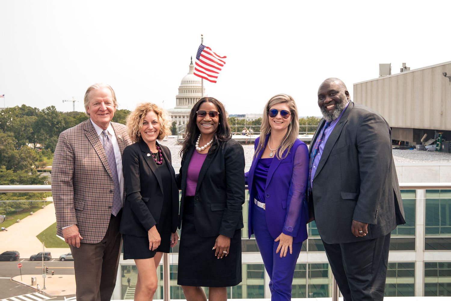 Professional group stands together on a rooftop terrace with an American flag visible in the background.