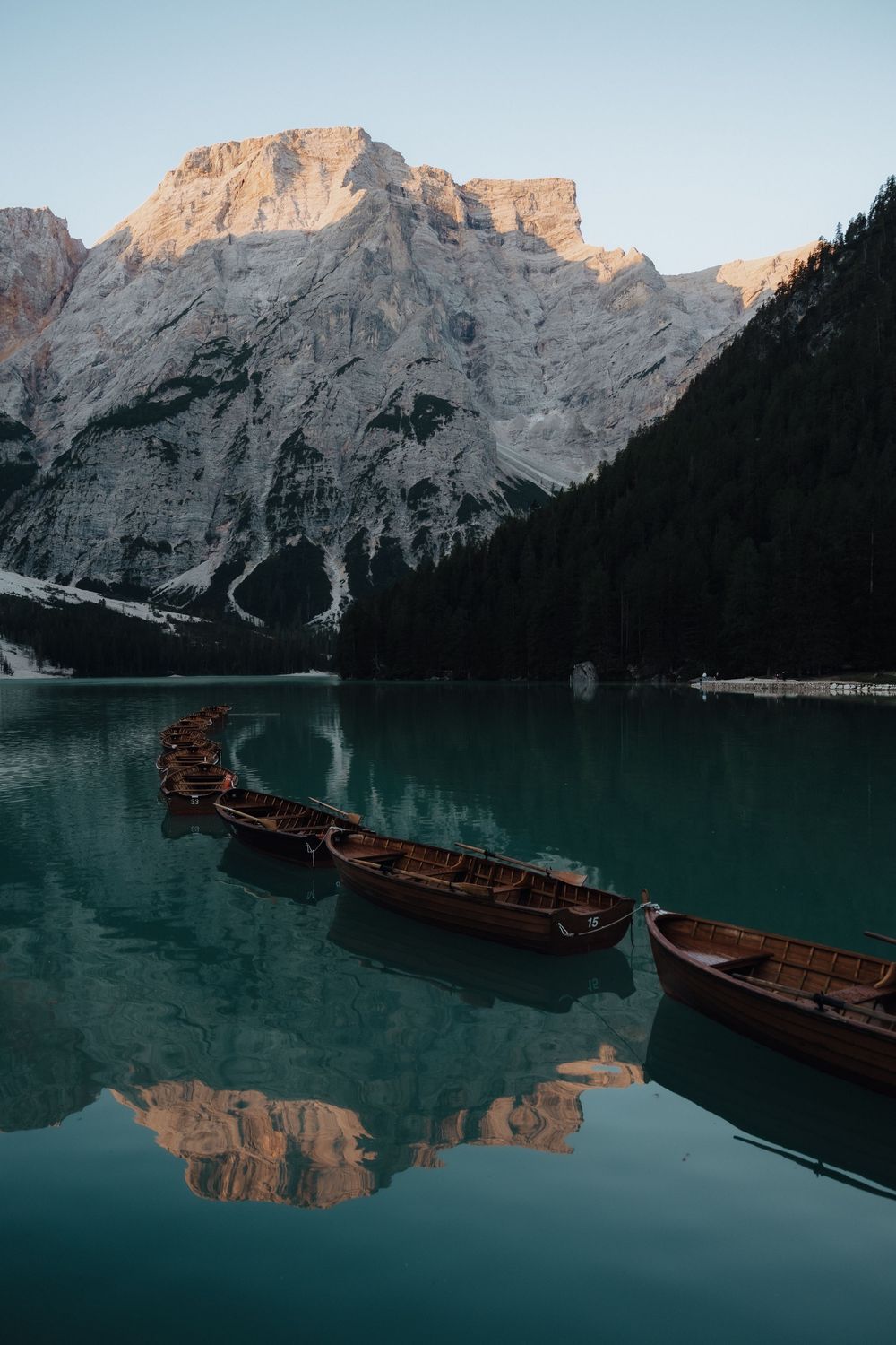 Wooden boats float on tranquil turquoise lake waters reflecting majestic Dolomite mountain peaks at sunset.