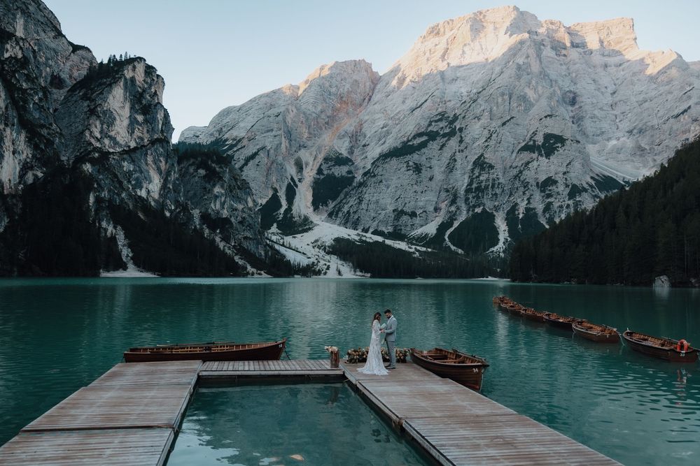 Wooden boats float on turquoise waters of Lake Braies surrounded by majestic Dolomite mountains in Italy at sunset.