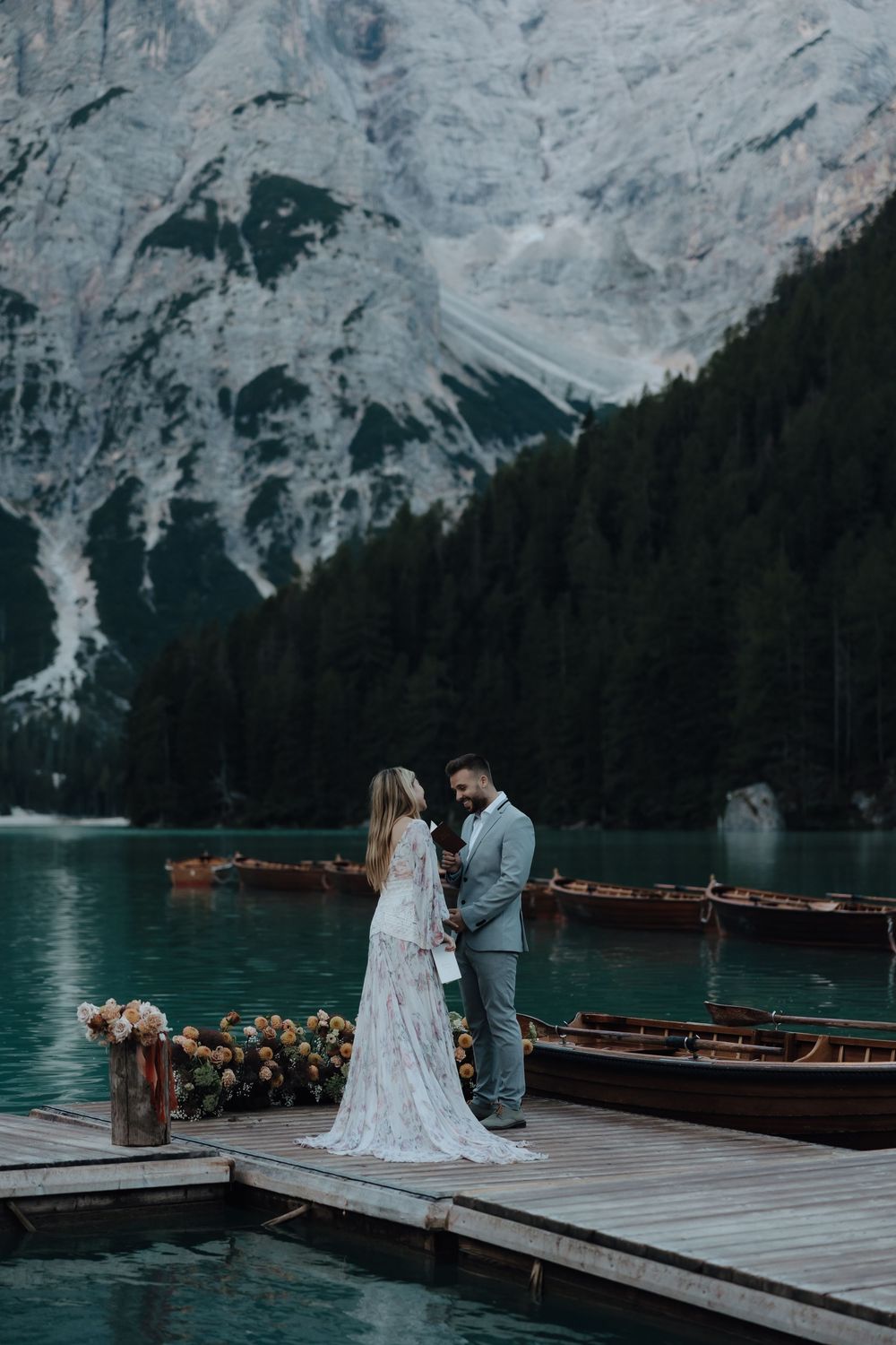 Romantic wedding couple photographs on wooden dock with stunning mountain lake and alpine scenery in Dolomites, Italy.