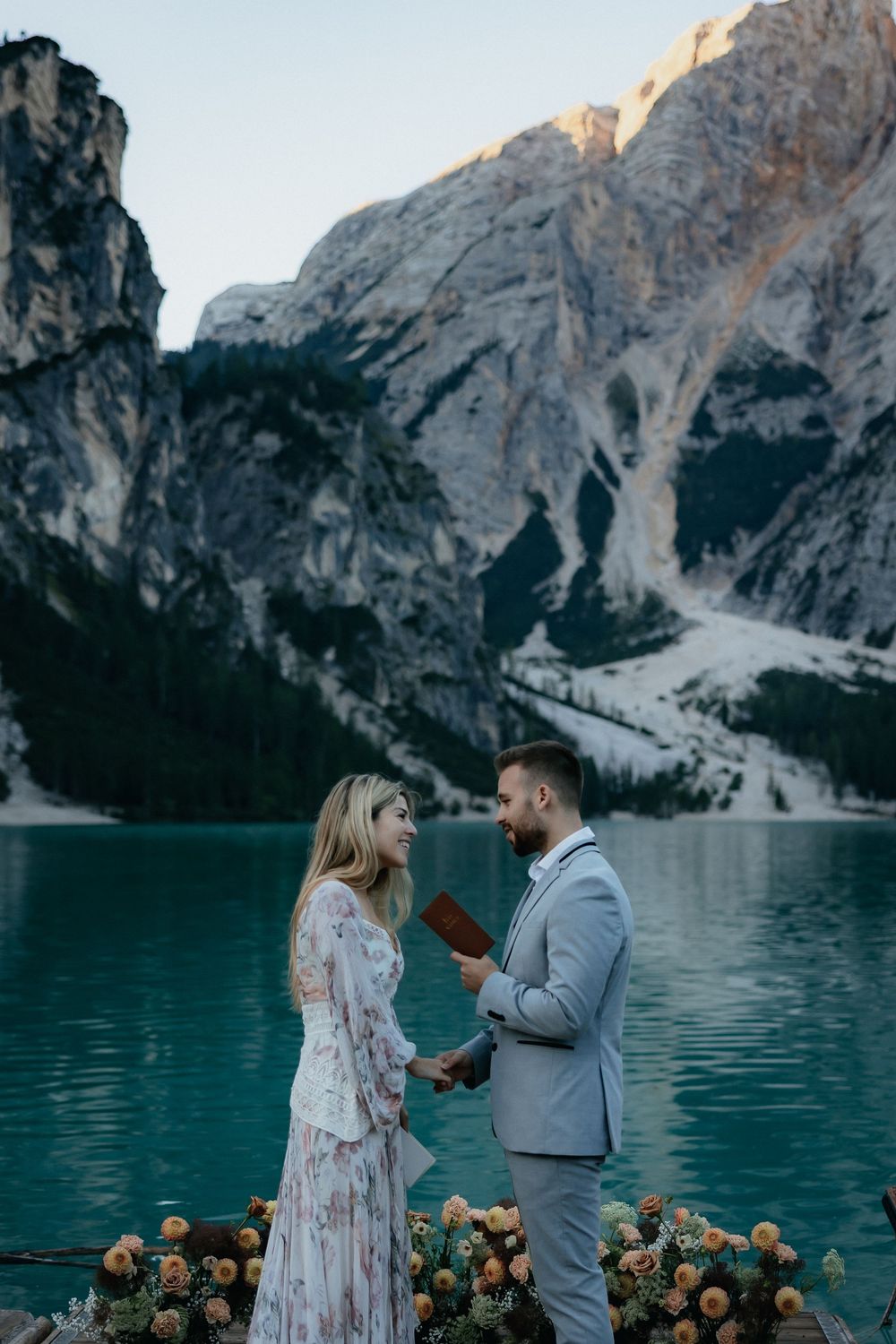 A romantic proposal scene at Lake Braies in the Dolomites with golden sunset light reflecting on turquoise waters and mountains.