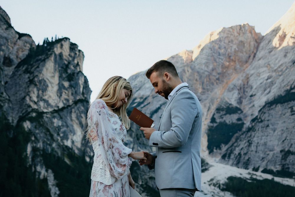 A couple embraces while hiking through dramatic mountain landscapes as the sun sets over the rugged peaks.