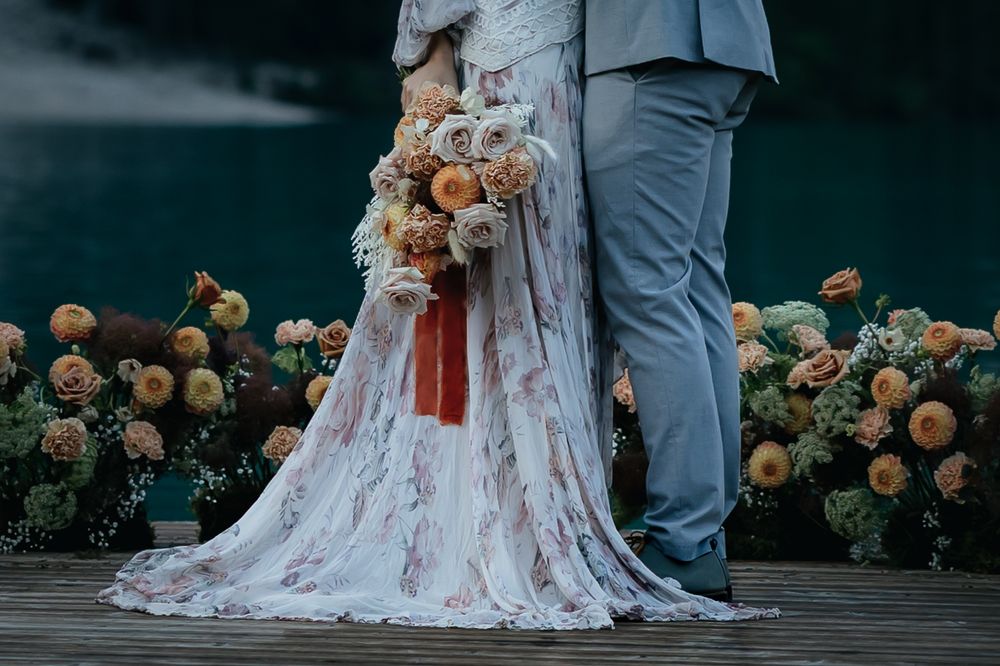 A row of wedding dress photographs showing the bottom of a gown with rose-colored floral decorations along a dark path.