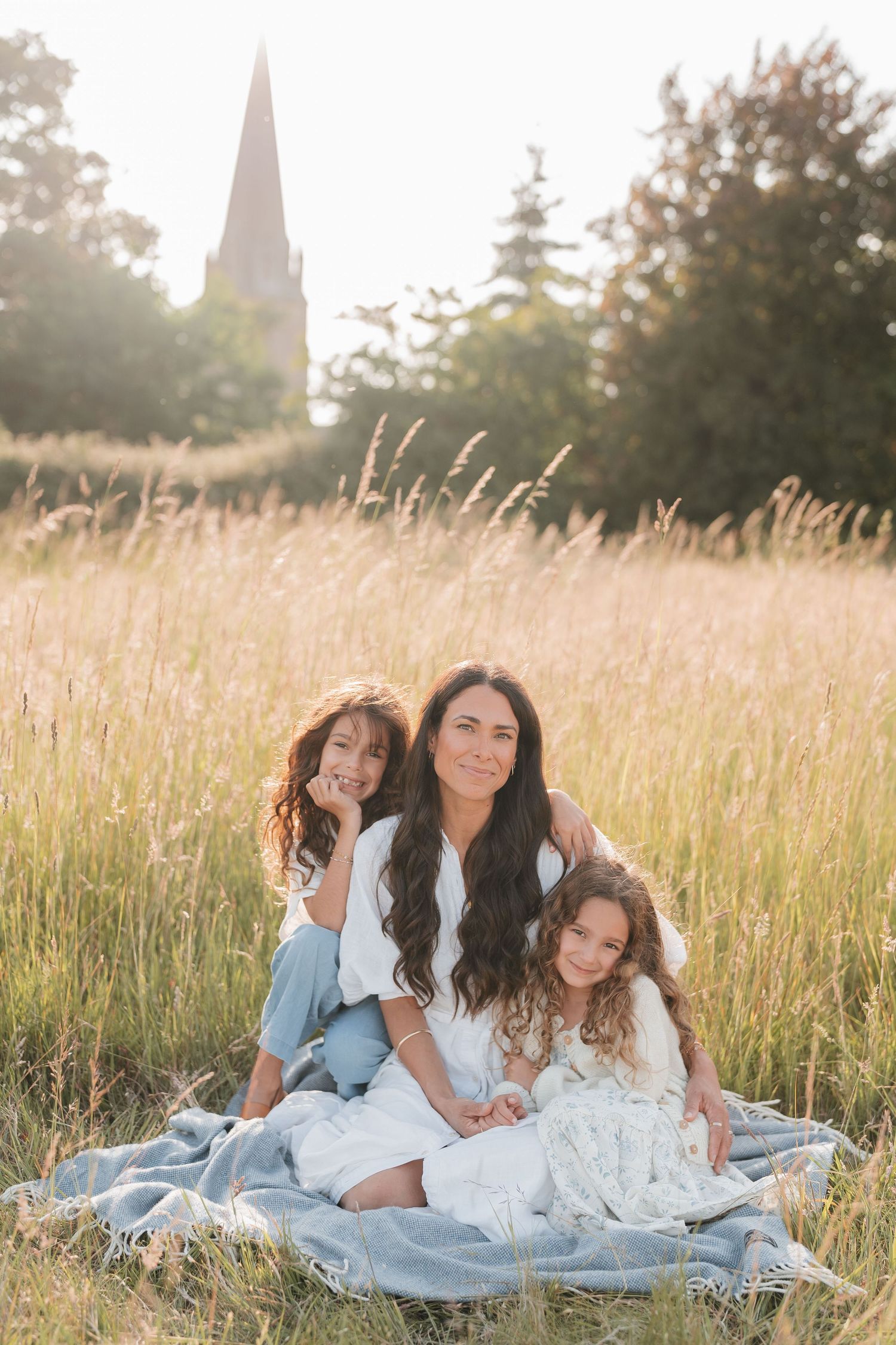Family members cuddle together on a white blanket in a summer field.