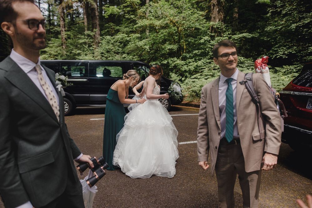 Wedding party members gather near parked cars on a forest path during an outdoor wedding celebration.