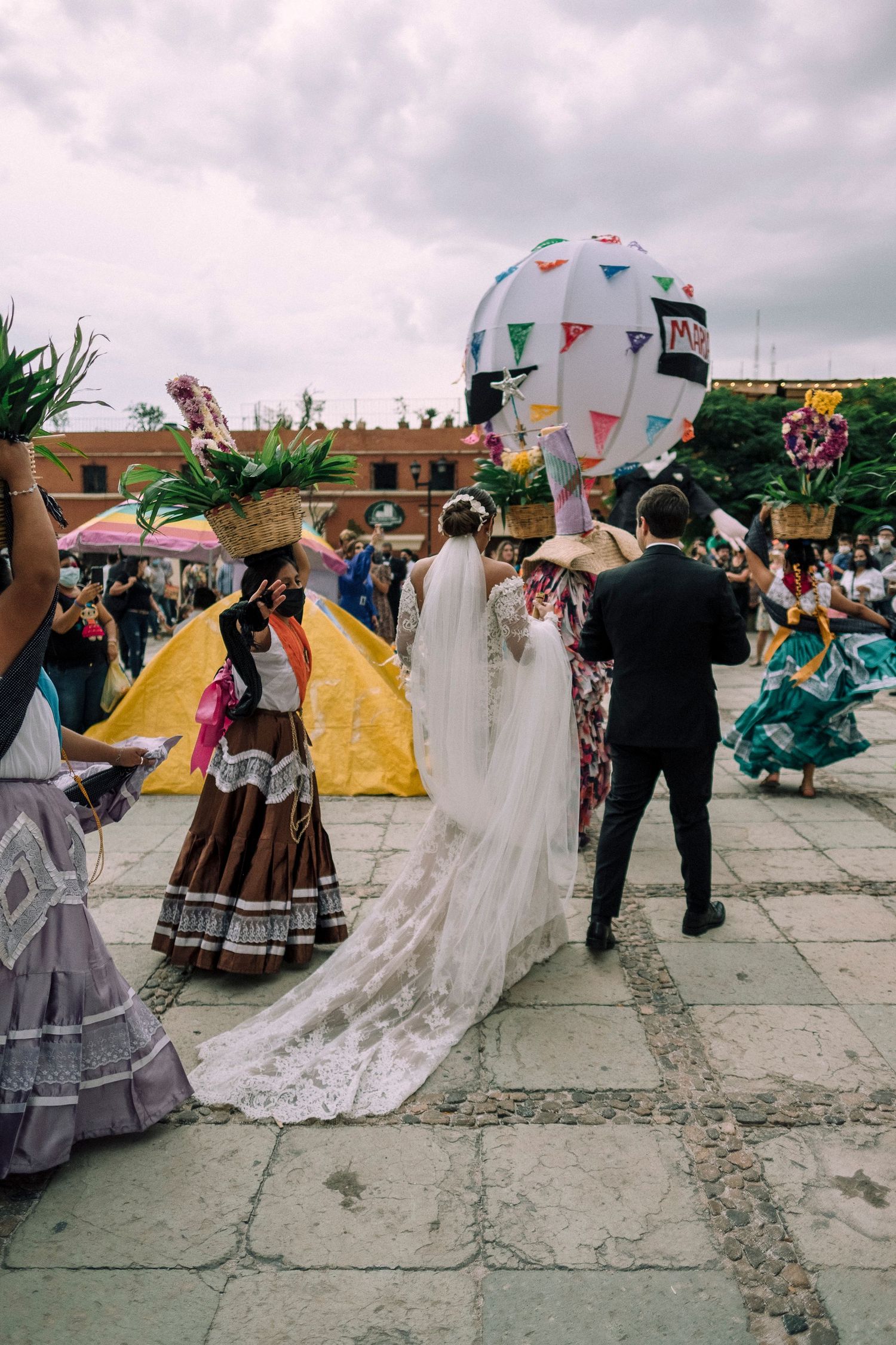 Wedding celebration in traditional dress with colorful flags and tents in an outdoor courtyard setting.