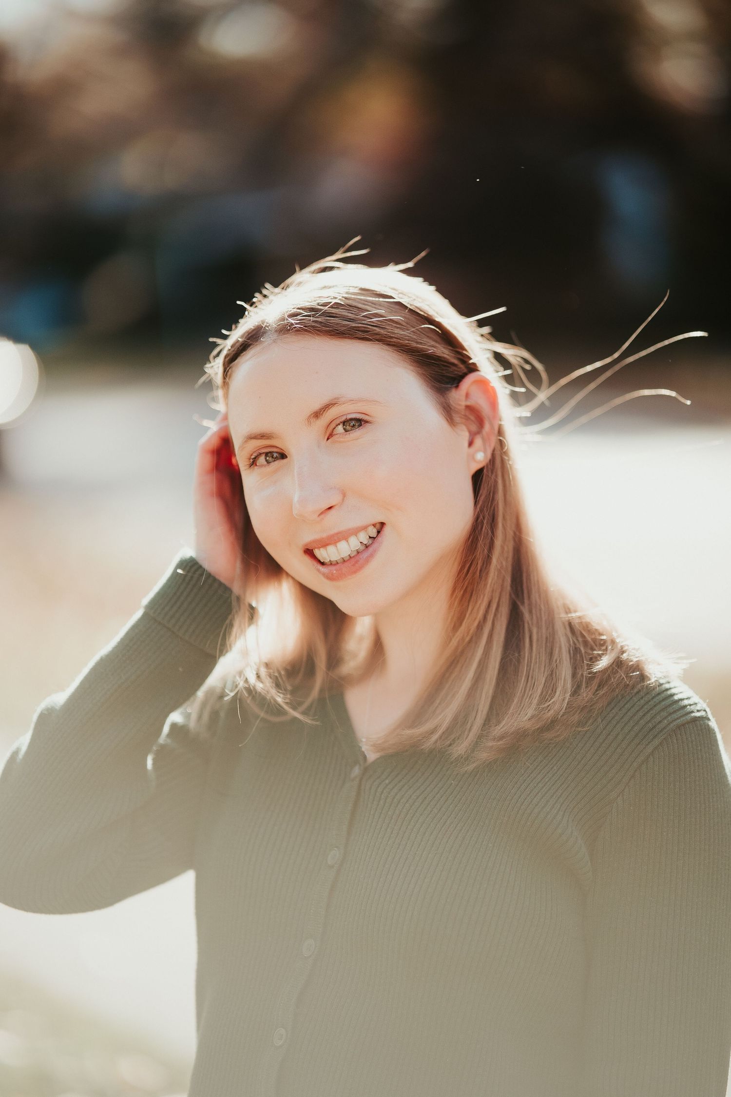 Close up portrait of someone wearing glasses, a beige turtleneck sweater and dark blazer smiling warmly outdoors.